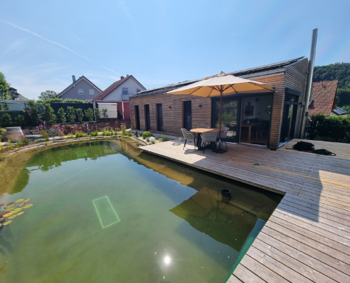 Moderner Holzrahmenbau mit Terrasse – Referenz Moderner Holzrahmenbau mit Holzterrasse und Naturpool im Garten