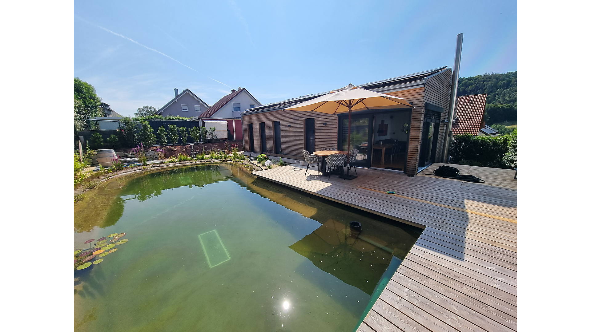 Moderner Holzrahmenbau mit Terrasse – Referenz Moderner Holzrahmenbau mit Holzterrasse und Naturpool im Garten